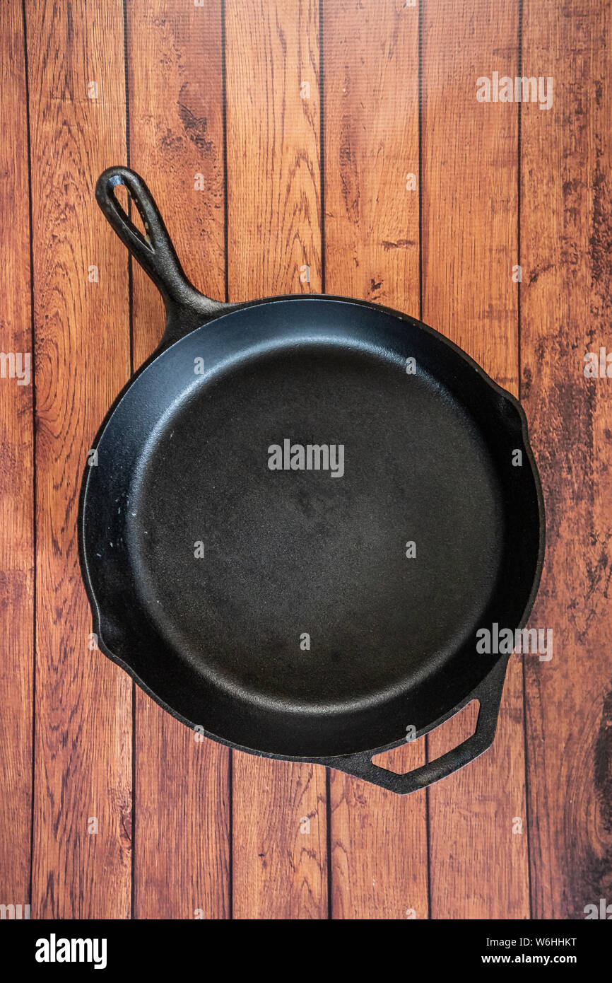 Traditional heavy duty cast iron skillet on wooden surface - isolated top view with copy space. Black cooking utensil - campfire cookware and kitchenw Stock Photo