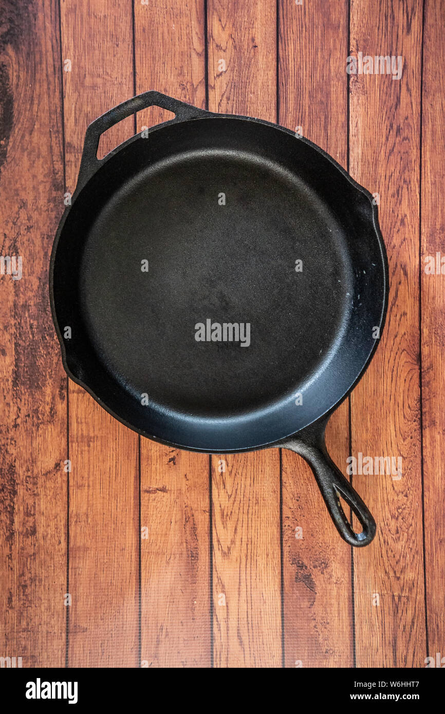Traditional heavy duty cast iron skillet on wooden surface - isolated top view with copy space. Black cooking utensil - campfire cookware and kitchenw Stock Photo