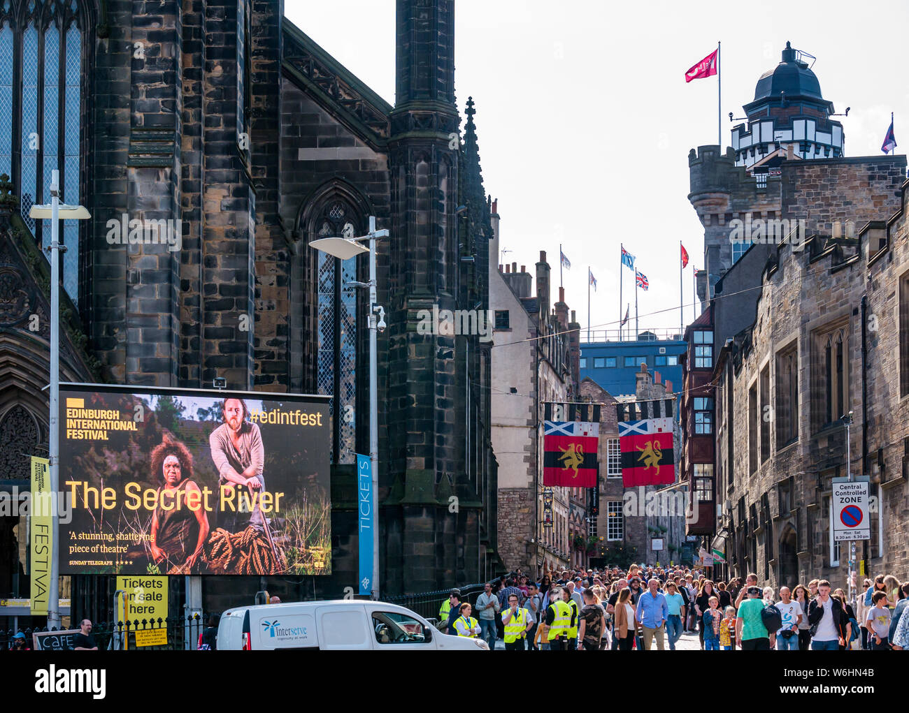 Royal Mile, Edinburgh, Scotland, United Kingdom, 1 August 2019. On the day before the official opening of the Fringe festival, the centre of the city along its main tourist route is already heaving with visitors. The headquarters of the Edinburgh International Festival, The Hub on Castlehill with a large poster advertising a drama play called The Secret River Stock Photo