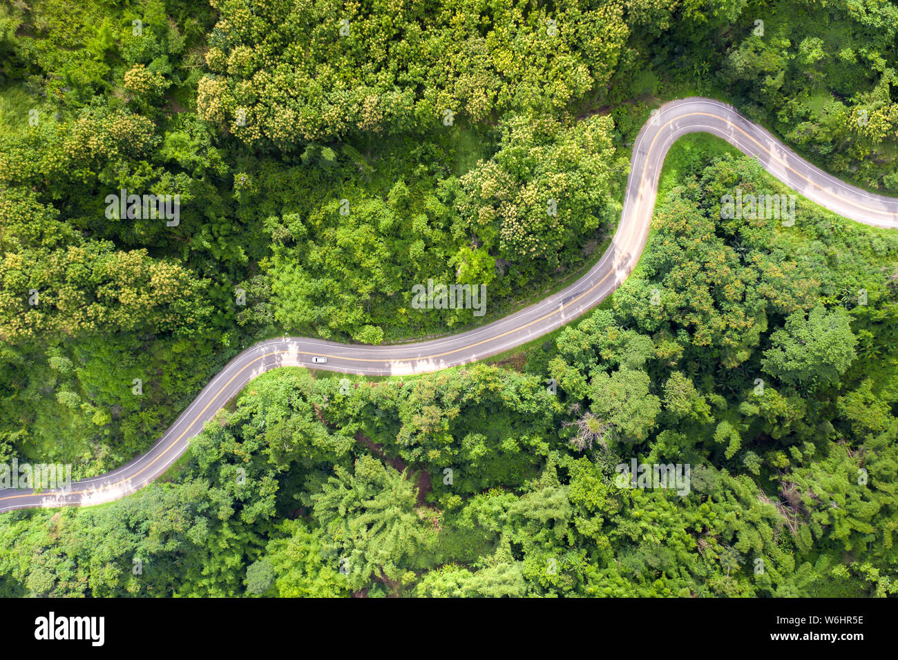 Aerial view over mountain road going through tropical rainforest landscape in Thailand. Stock Photo