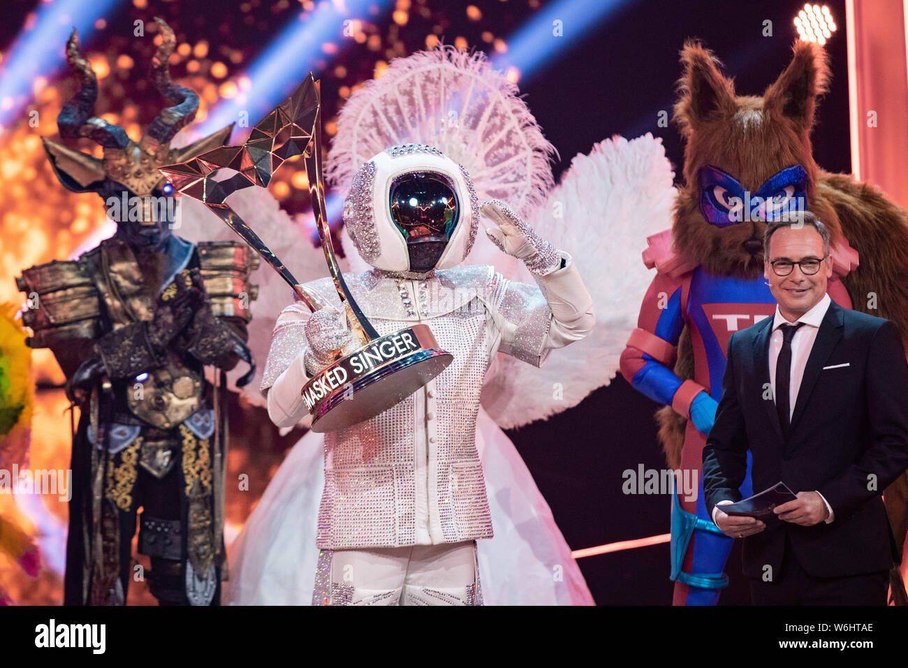 Cologne, Germany. 02nd Aug, 2019. The winner of the ProSieben show "The Masked  Singer", Max Mutzke (M), cheers as "astronaut" with his trophy on stage. To  his right is moderator Matthias Opdenhövel.