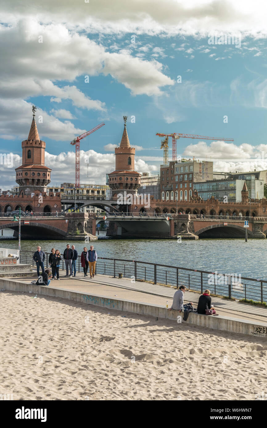 BERLIN, GERMANY - September 26, 2018: Panorama of Berliners sitting by the Spree river, near the East Side Gallery with the Oberbaum Bridge in the Stock Photo