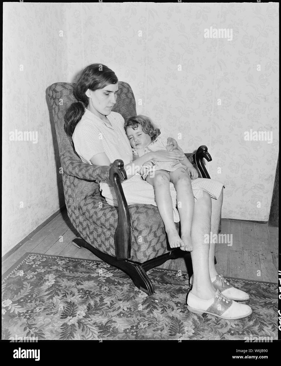 Lucy Sergent, who is blind, rocks her sister Bobbie Jean to sleep. Great devotion and family feeling among the parents and children in this family was evident. The older children helped the youngsters with their lessons; the boys always walked home with their younger sisters from school; the boys brought home nuts from the woods for the younger girls, etc. P V & K Coal Company, Clover Gap Mine, Lejunior, Harlan County, Kentucky. Stock Photo