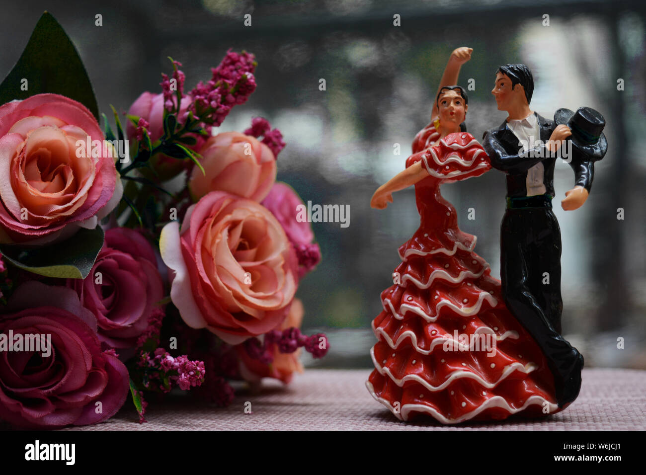 Close up of two flamenco dancers, both male and female. Figurines or souvenirs placed next to a bouquet of pink roses. Stock Photo