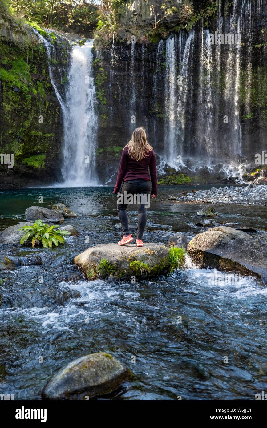 Young woman standing on a stone in a river, Shiraito Waterfall, Yamanashi Prefecture, Japan Stock Photo