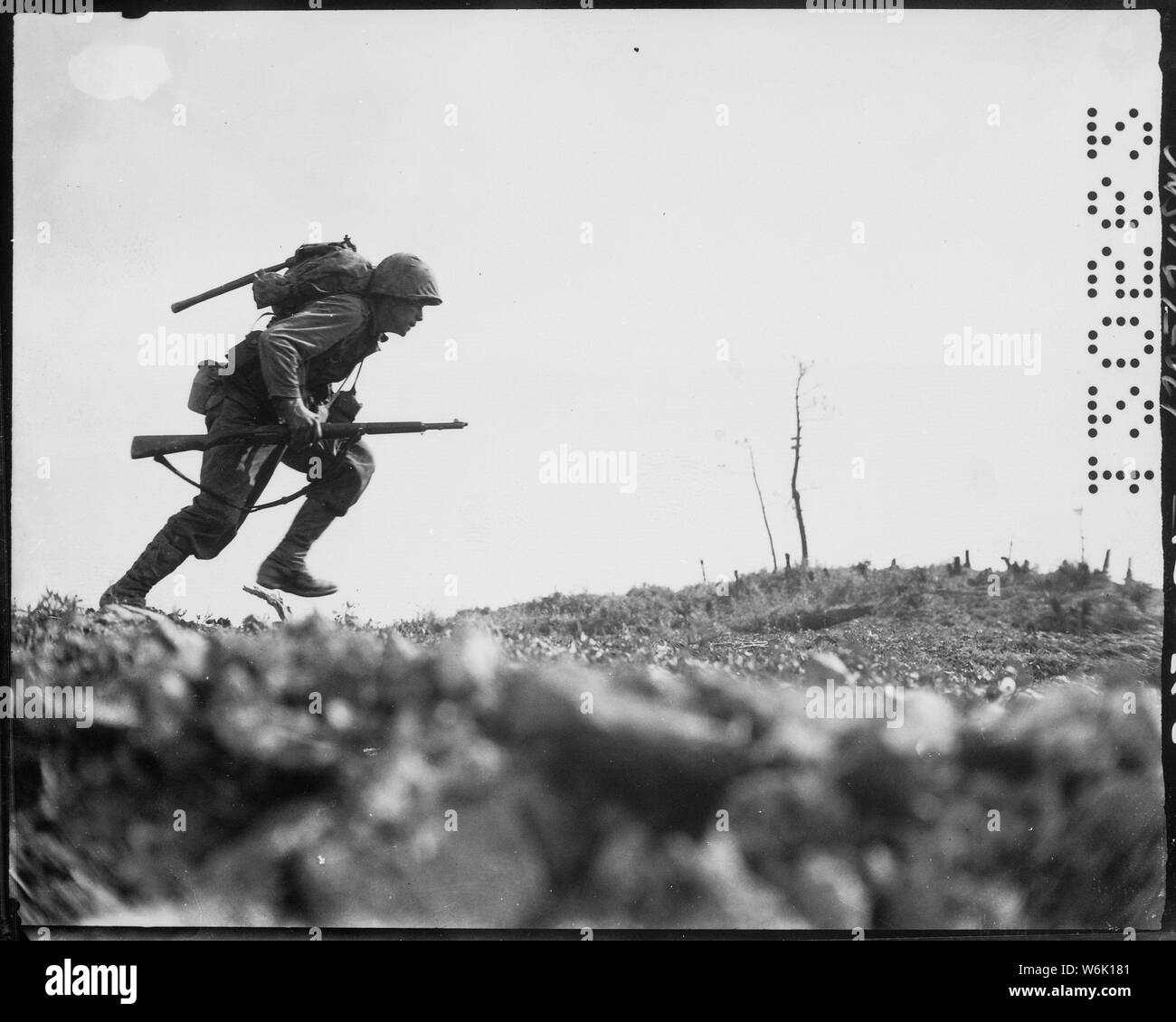 Photograph of a Marine Charging Japanese Machine Guns on Okinawa; Scope and content:  Original caption: A Marine dashes through Japanese machine gun fire while crossing a draw, called Death Valley by the men fighting there. Marines sustained more than 125 casualties in eight hours crossing this valley. Okinawa, May 10, 1945. Stock Photo