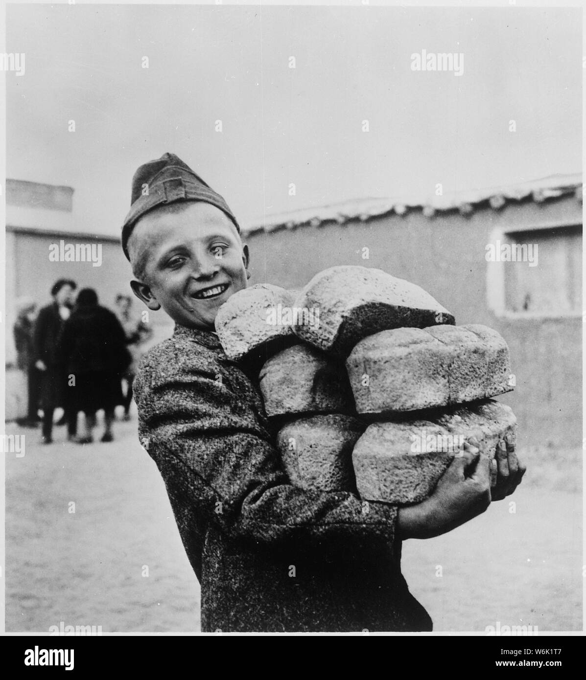 Polish youngster with his arms loaded down with bread made from flour supplied by the American Red Cross. He is smiling in anticipation of enough bread to eat, something what was unimaginable in soviet gulags, where he probably spent some time after deportation with family from Eastern Poland, occupied by Red Army in 1939. Hunger and barely enough food to stay alive was norm in soviet work camps.; General notes:  Use War and Conflict Number 1256 when ordering a reproduction or requesting information about this image. Stock Photo