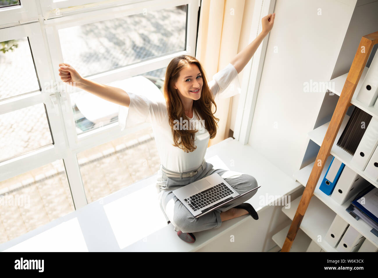 An Elevated View Of A Businesswoman Sitting Over Cabinet Stretching Her Arms Stock Photo