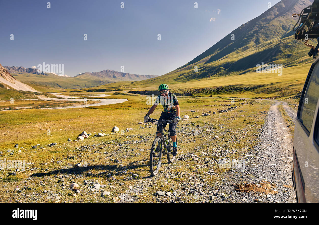 Man on mountain bike rides on the road in the green mountain valley. Stock Photo