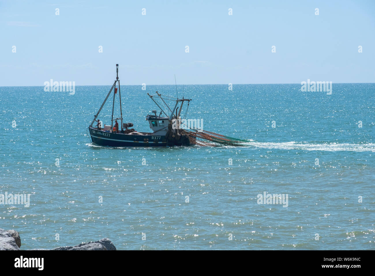 Hastings fishing trawler returning to Harbour with trawl nets out close to shore, East Sussex, UK Stock Photo