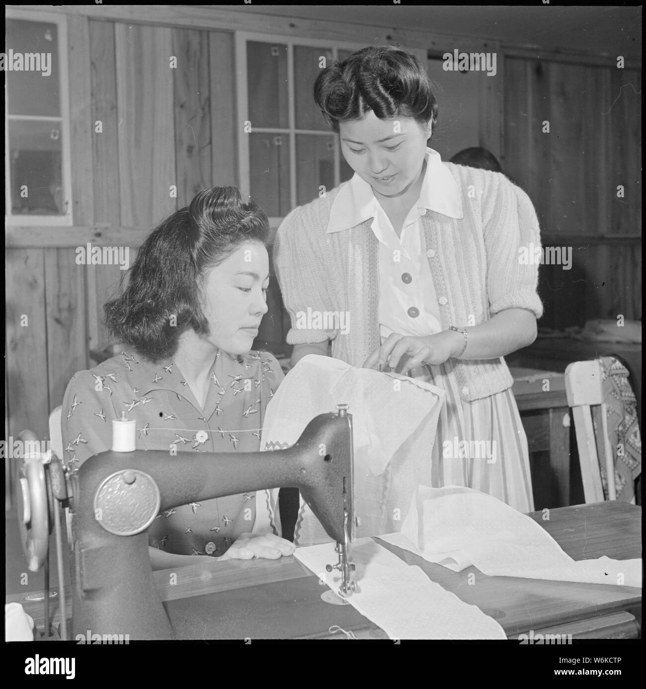 Rohwer Relocation Center, McGehee, Arkansas. In a sewing class at the Rohwer Center schools, Misaye . . .; Scope and content:  The full caption for this photograph reads: Rohwer Relocation Center, McGehee, Arkansas. In a sewing class at the Rohwer Center schools, Misaye Oku gets pointers from istructress, Mrs. Sadako Yasue. Adult classes, teaching subjects which contribute to the comforts or living requirements of center life, are very popular with house-wives and mothers. Stock Photo
