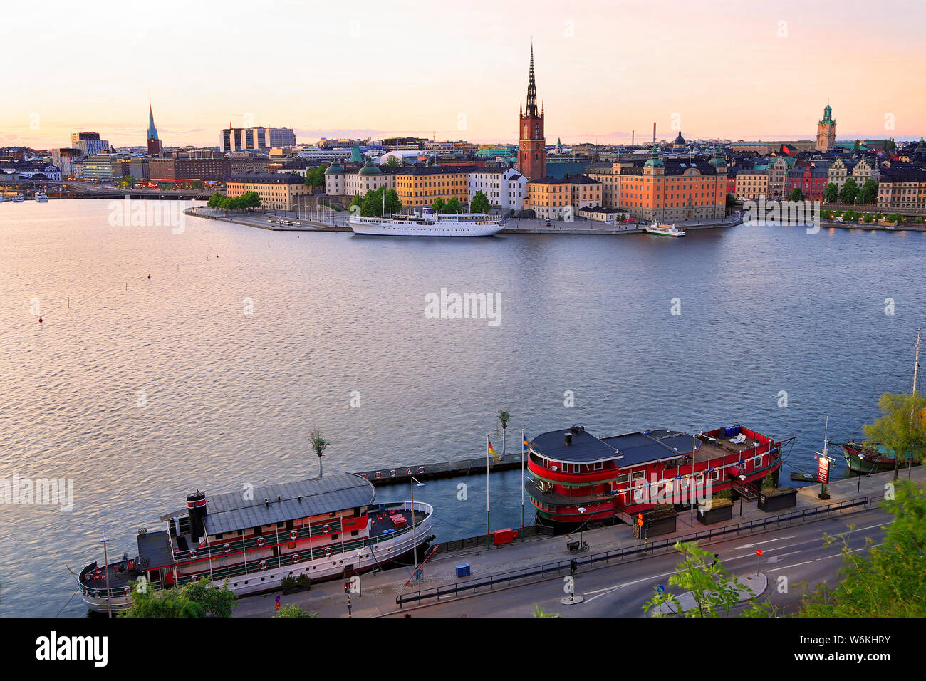 Scenic view of Stockholm's skyline including Gamla Stan illuminated at dusk with colorful boats on the foreground, Sweden Stock Photo