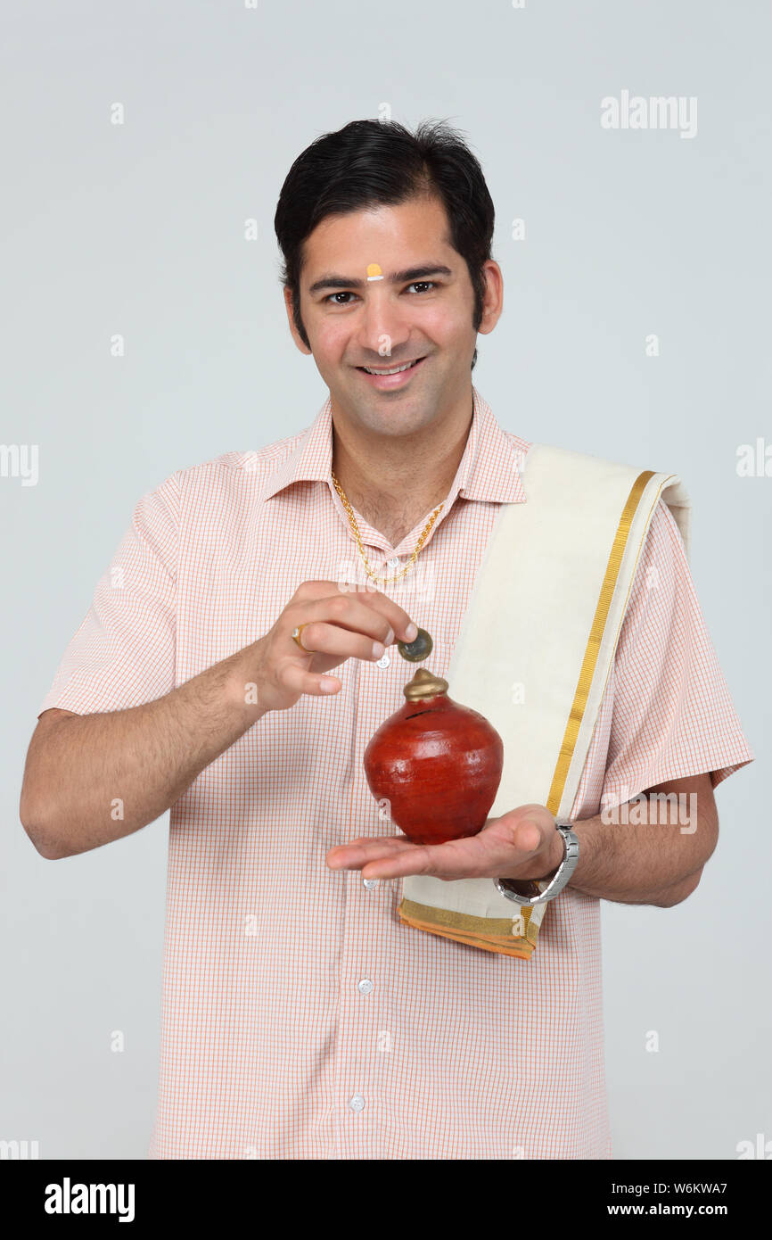 South Indian man inserting a coin into a piggy bank Stock Photo - Alamy