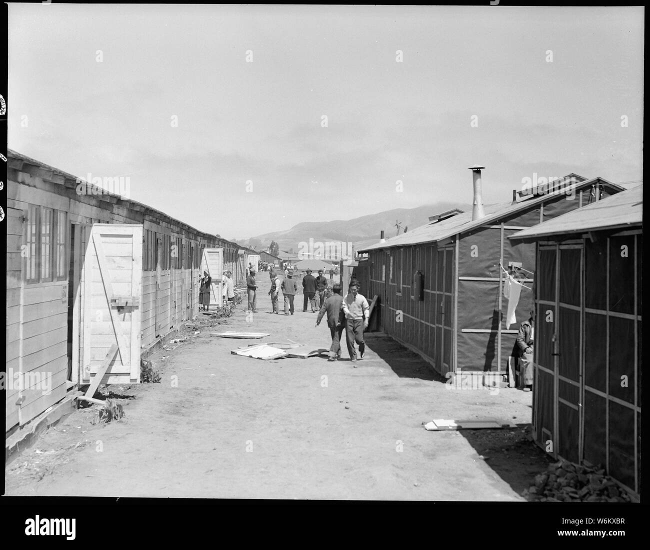 San Bruno, California. Looking down one of the avenues between rows of barracks. The ones on the r . . .; Scope and content:  The full caption for this photograph reads: San Bruno, California. Looking down one of the avenues between rows of barracks. The ones on the right are converted horse stalls, and those on the left are newly contructed and typical of an assembly center and relocation centers throughout the west. They are 100 feet long, covered with black tar paper, contain five 1-room apartments, each of which accomodate a family. The attitudes of the people in this photograph are typica Stock Photo