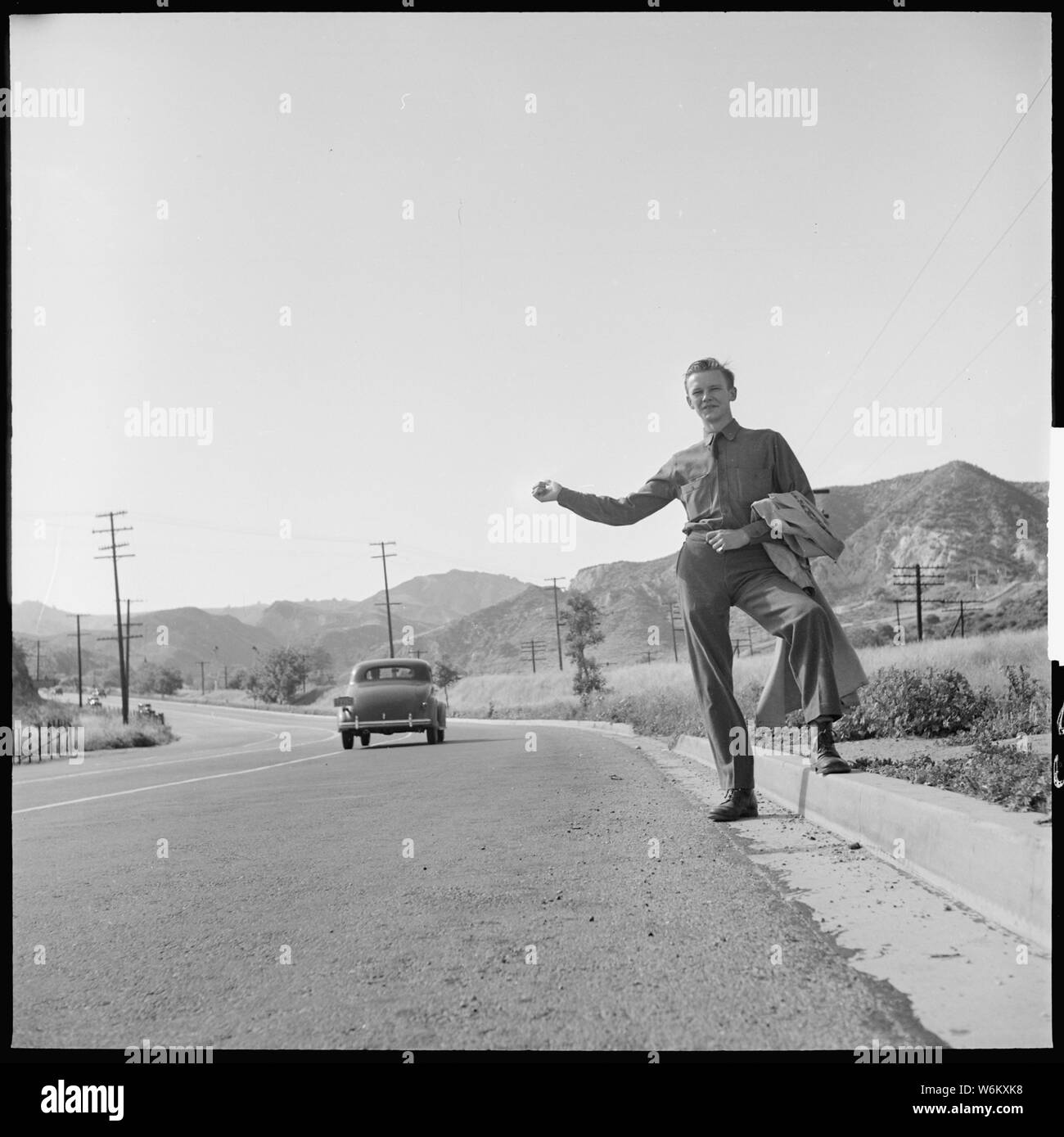 San Fernando, California. Hitch-hiking. This Civilian Conservation Corps boy is returning to camp about thirty miles away after a weekend visit to his family in Los Angeles; General notes:  — Near Newhall Pass (Ridge Route of Hwy 99) in Sylmar, at the Santa Susana Mountains in the northern San Fernando Valley, Los Angeles, California (1940). Stock Photo