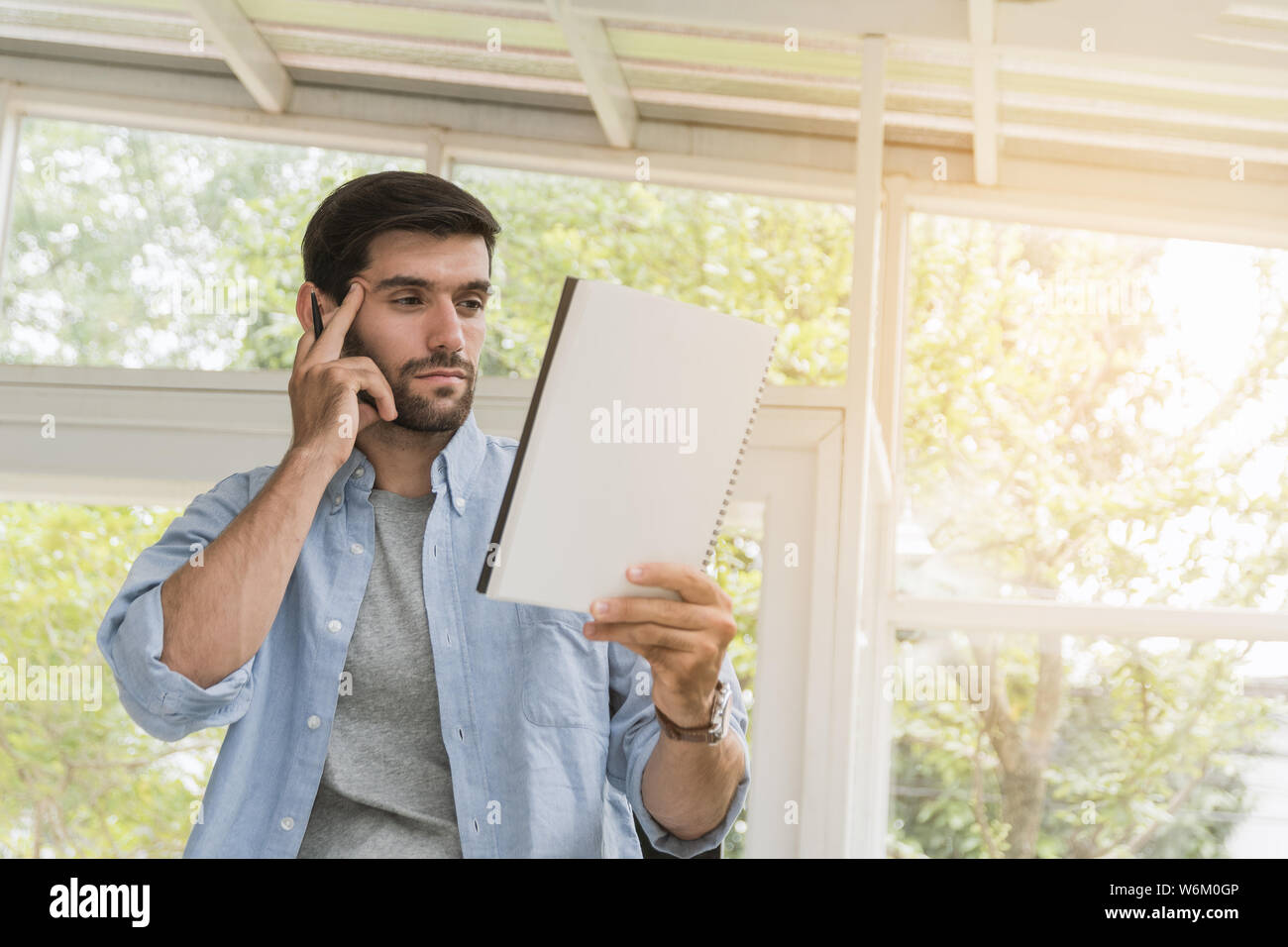 Handsome man have beards wear gray t-shirt and wear a blue shirt over the outside, wearing wrist watch in hand holding a notebook and pen, are using t Stock Photo