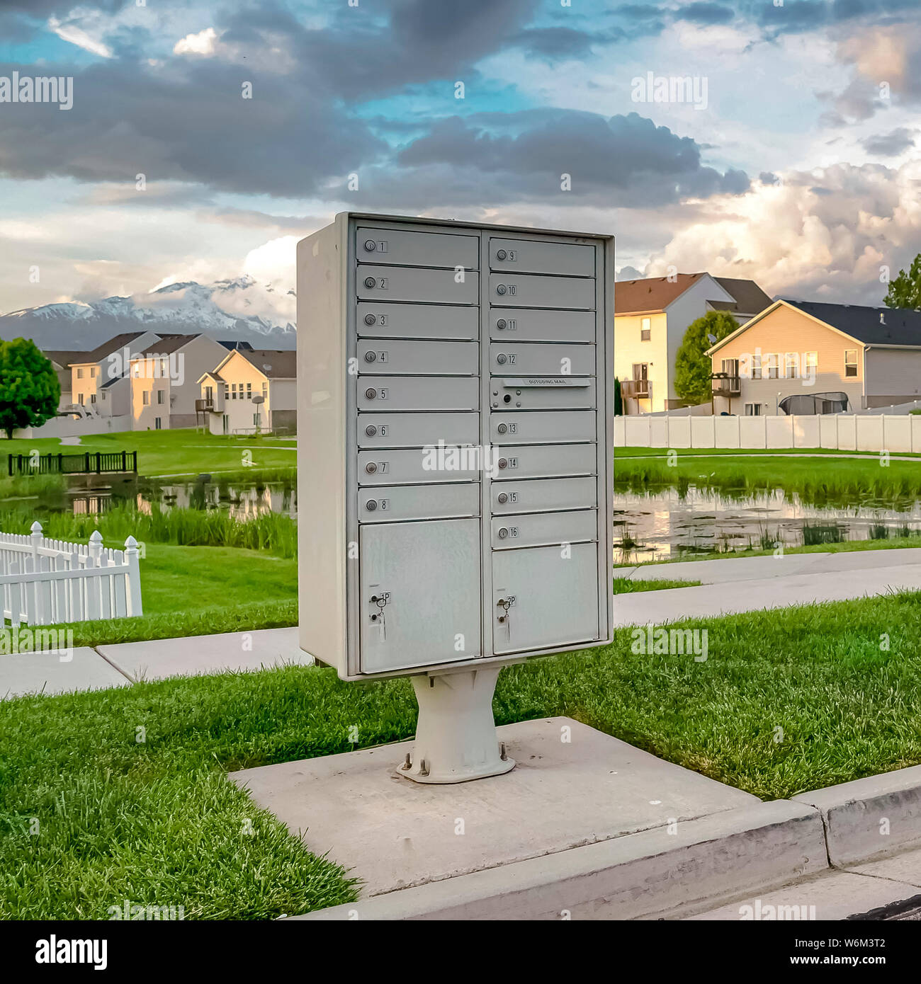 Square Mailbox on the side of the road with pond grassy terrain and homes background Stock Photo