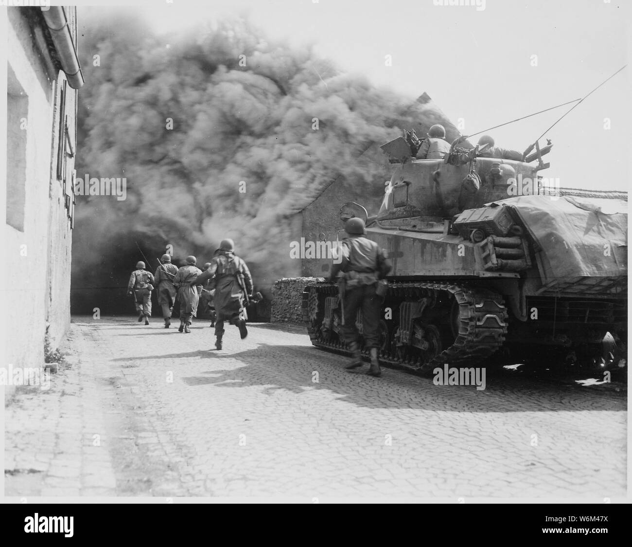 Soldiers of the 55th Armored Infantry Battalion and tank of the 22nd Tank Battalion, move through smoke filled street. Wernberg, Germany.; General notes:  Use War and Conflict Number 1094 when ordering a reproduction or requesting information about this image. Stock Photo