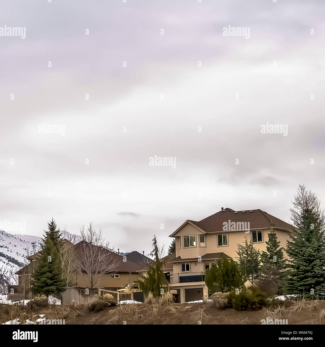 Square Vast cloudy sky over residential area built on snowy hill with coniferous trees Stock