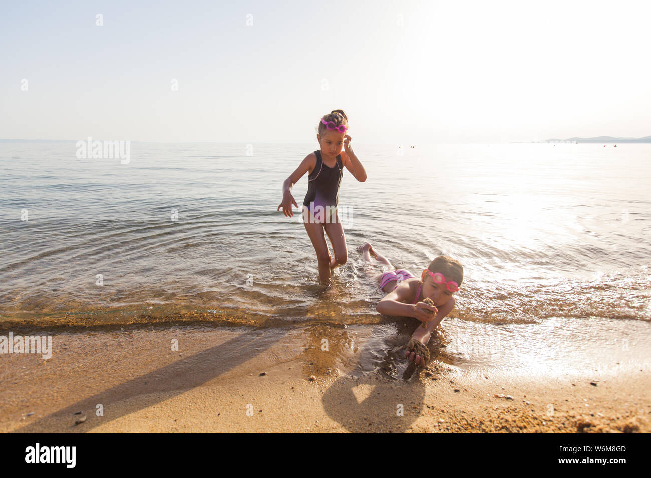 Happy children fun on sand beach at summer vacation. Little girls wearing swimming goggles Stock Photo