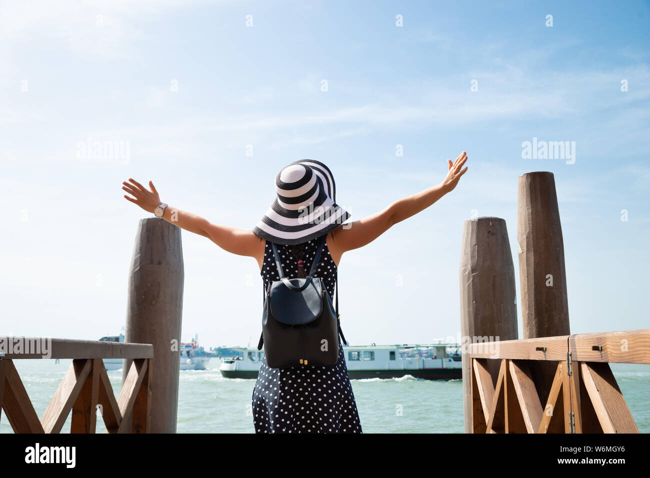 Rear View Of A Female Tourist Outstretching Hands Standing On Pier Enjoying Vacation In Venice Stock Photo