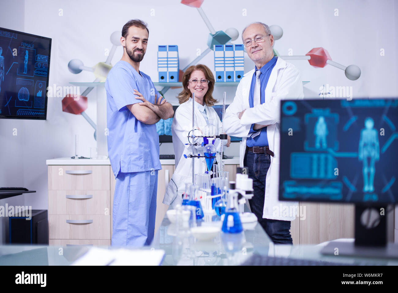 Smiling scientist colleagues in their uniform standing in chimical lab. Laboratory equipment. Stock Photo