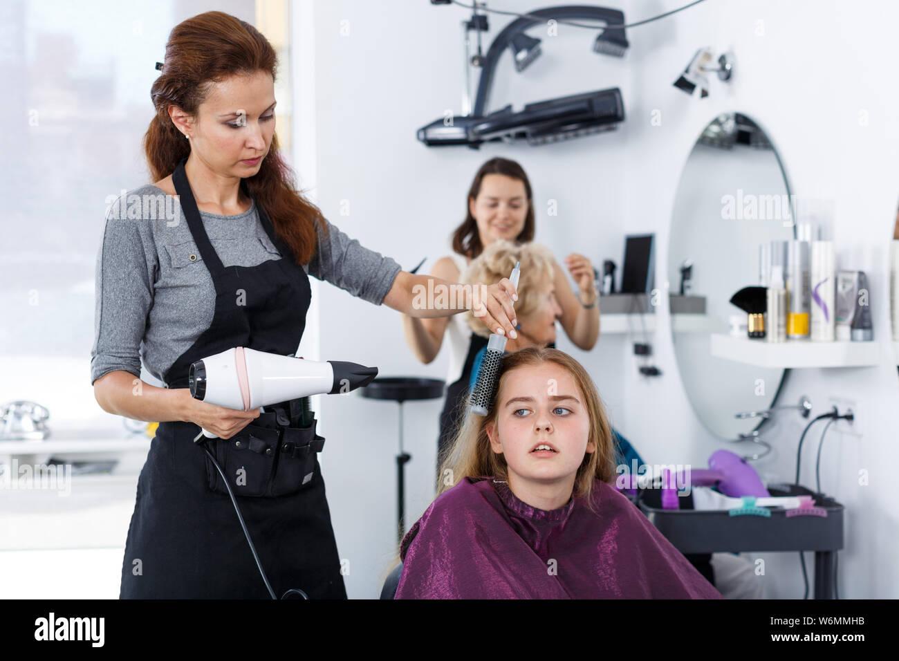 Hairdresser drying long brown hair of teen girl with hair dryer and ...