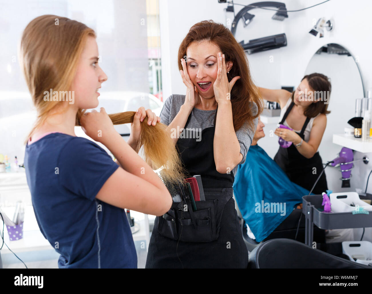 Shocked woman hairdresser looking at hair of young female client ...