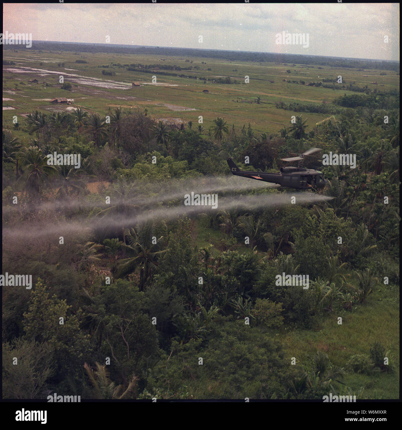 Vietnam. Defoliation Mission. A UH-1D helicopter from the 336th Aviation Company sprays a defoliation agent on a dense jungle area in the Mekong delta.; General notes:  The photo is inverted. Stock Photo