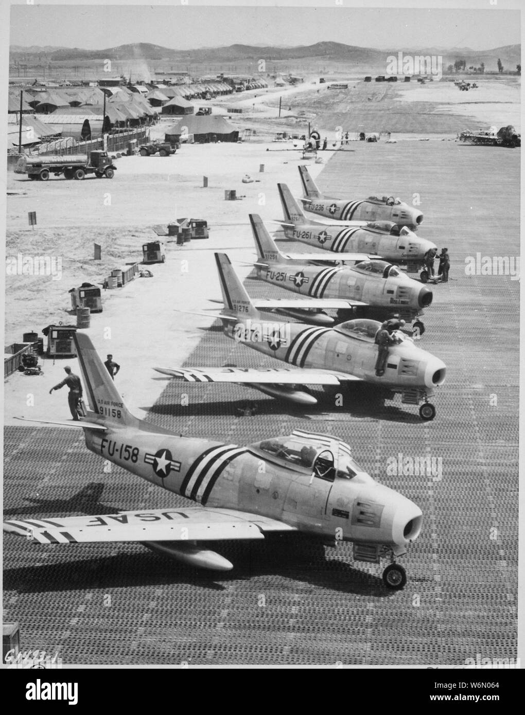 View of F-86 airplanes on the flight line getting ready for combat. Air Force.; General notes:  Five North American F-86A Sabre fighters of the 4th Fighter Interceptor Wing on the flight line at Suwon, South Korea, in June 1951. The F-86As were F-86A-5-NA: 49-1158 was damaged by a MiG-15 on 23 September 1951; 49-1276 of the 336th FIS was shot down by a MiG-15 on 22 June 1951; 49-1251; 49-1261; 49-1236 of the 334th FIS was shot down by a MiG-15 on 24 October 1951.  Use War and Conflict Number 1413 when ordering a reproduction or requesting information about this image. Stock Photo