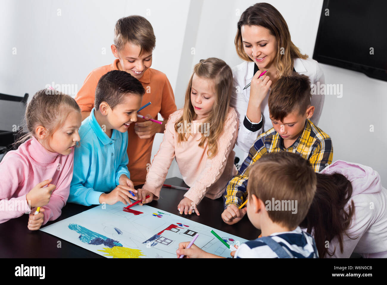 Little smiling children with teacher drawing together in classroom ...