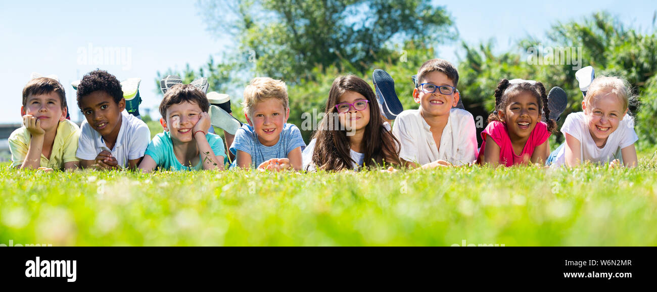 Group of happy children resting on grass and smiling together in park ...