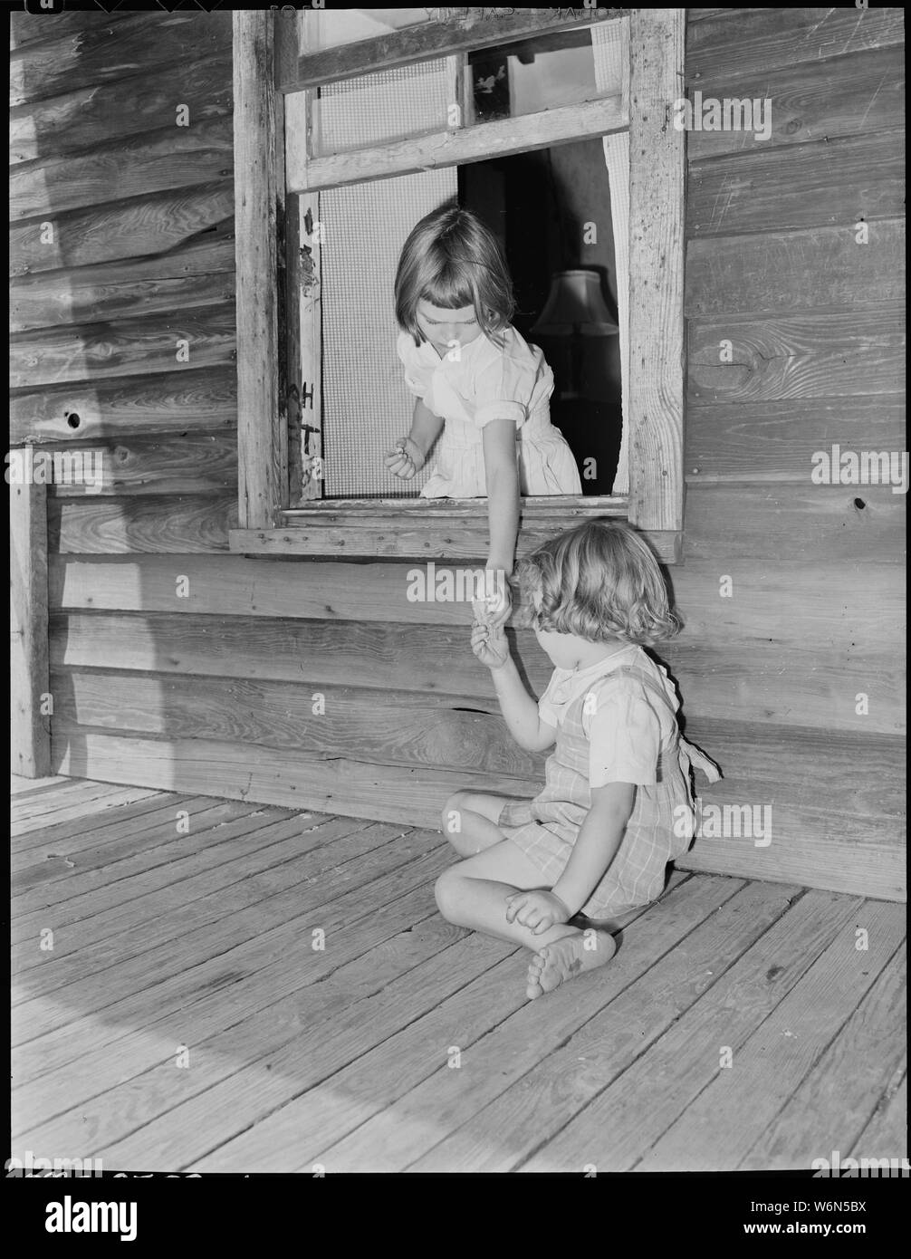 Wanda Lee Sergent hands her sister, Bobbie Jean, an ice cream cone through  the window opening from the front porch to the living room of their home.  No screening of windows nor