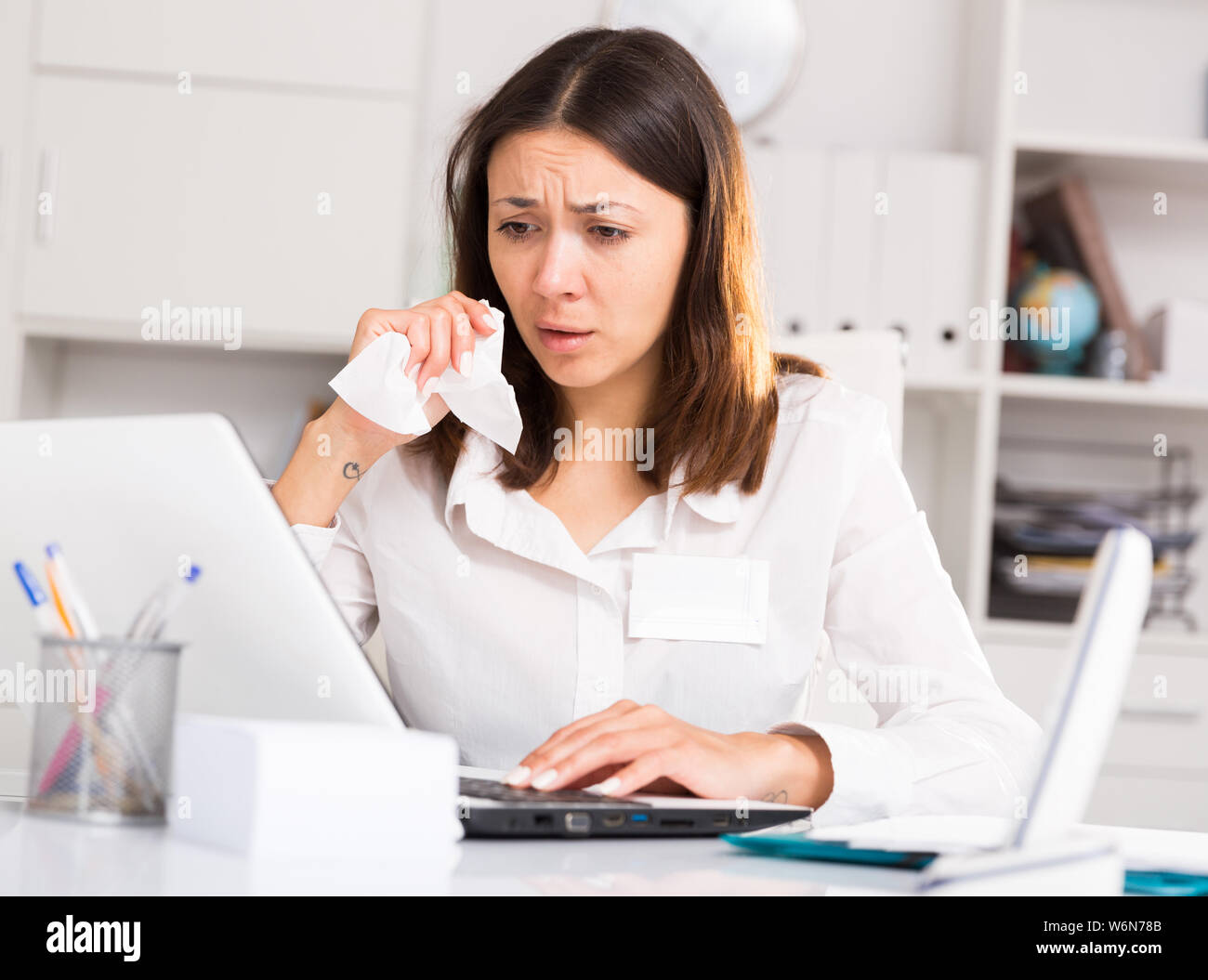 Unhappy girl  holding napkin  during work with laptop and documents in office Stock Photo