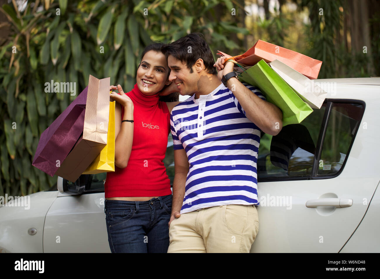 Couple leaning against a car with shopping bags Stock Photo