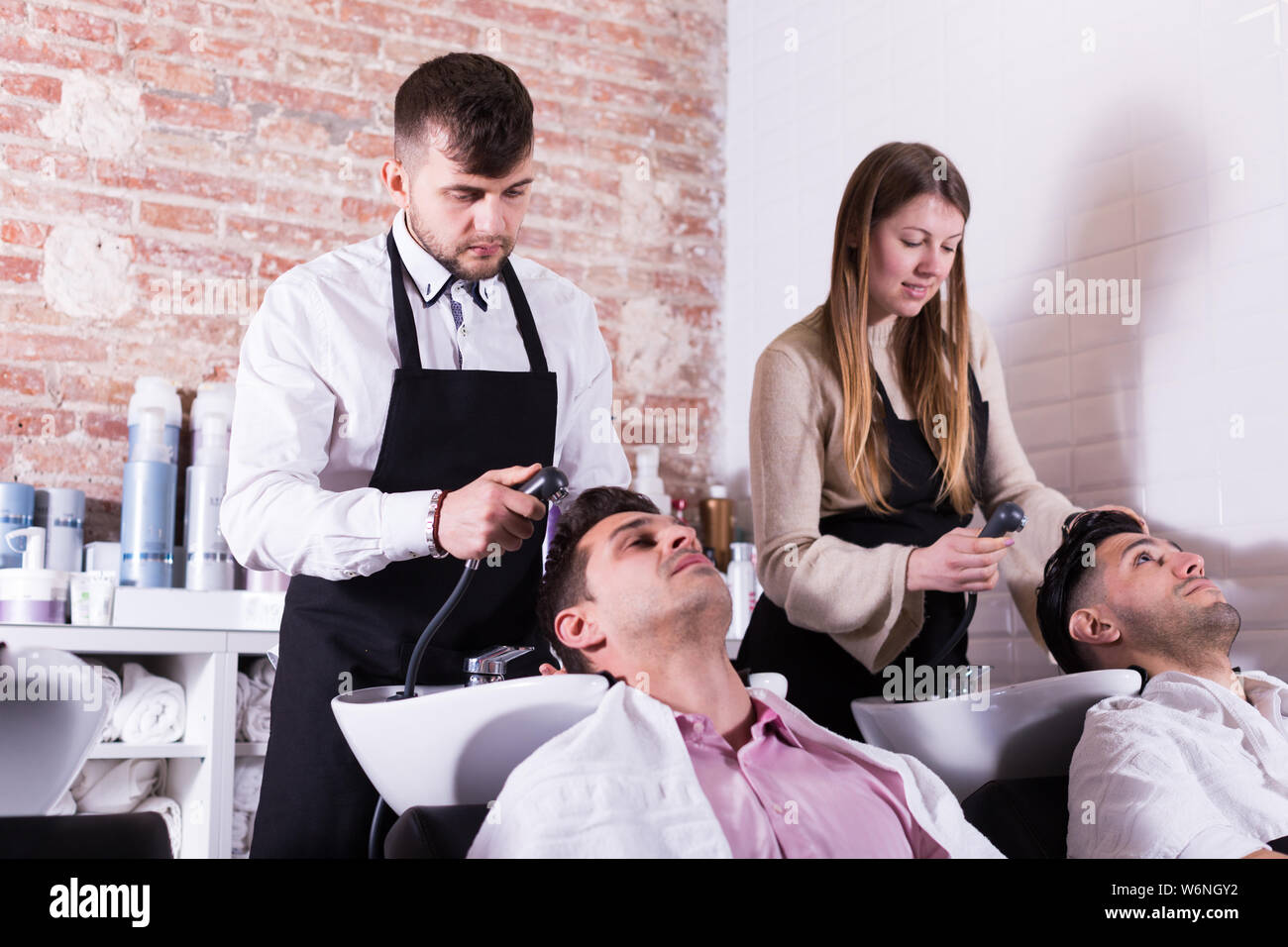Men Leaning Heads On Sink And Relaxing While Hairdressers Washing