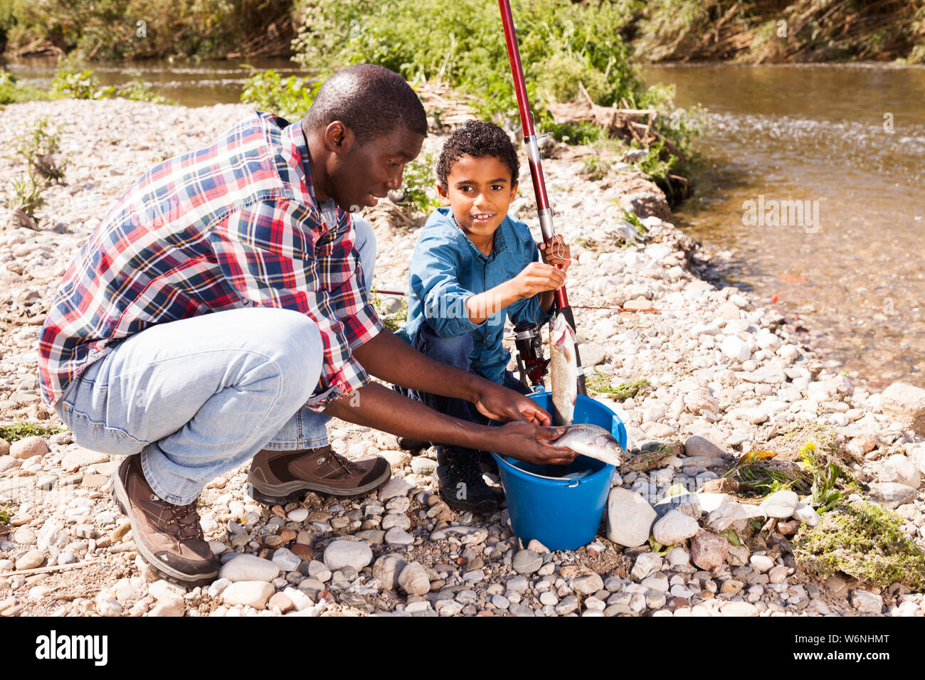 Portrait of enthusiastic little African boy and his father holding fishing rod with fish on hook Stock Photo