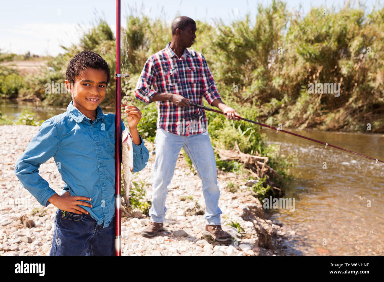 Portrait of afro fisherman and his little son holding fishing rod with fish on hook Stock Photo