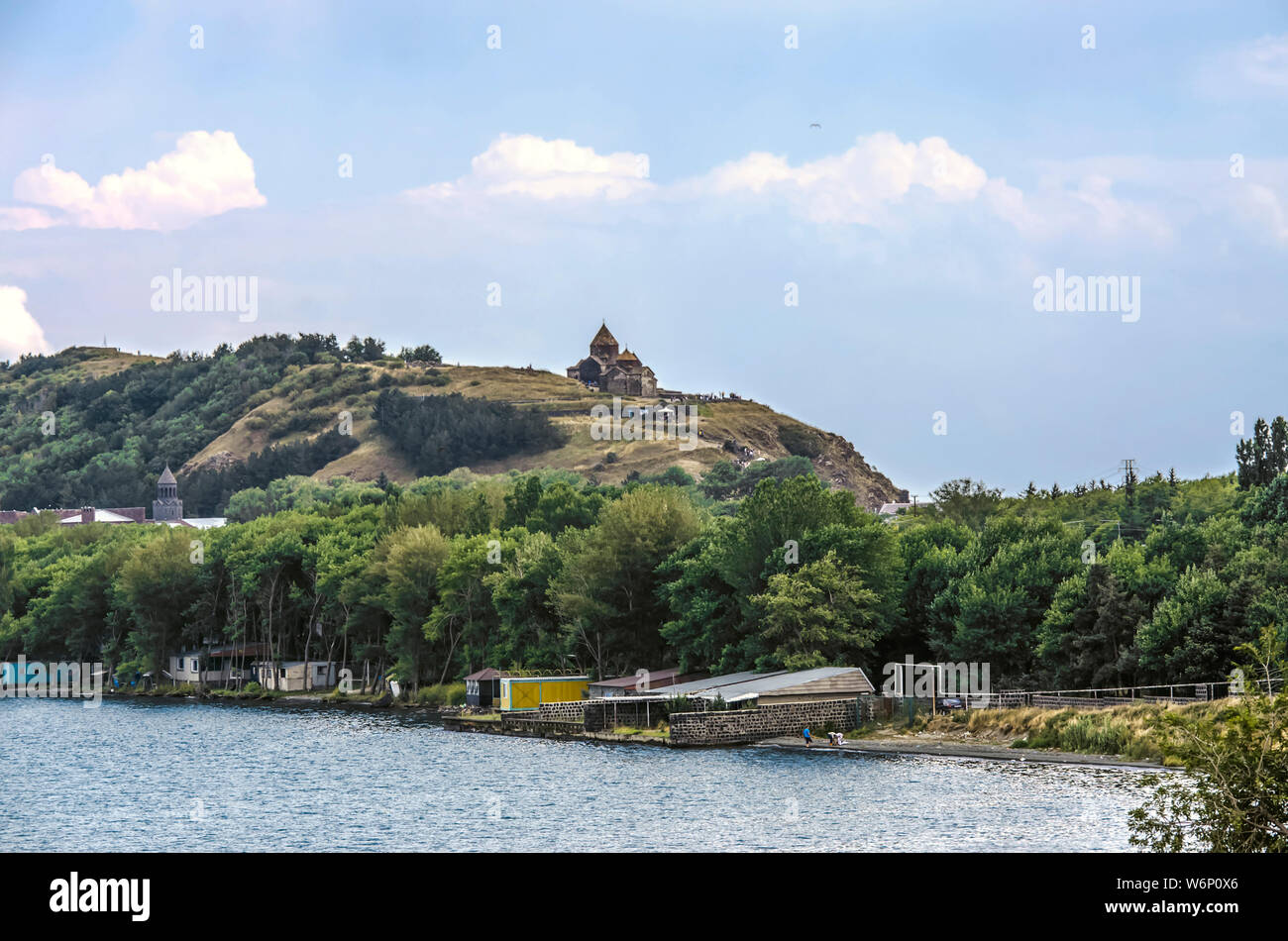 Shore on the peninsula of lake Sevan, with buildings among trees and the hill with the medieval monastery of Sevan in the Gegharkunik province of Arme Stock Photo