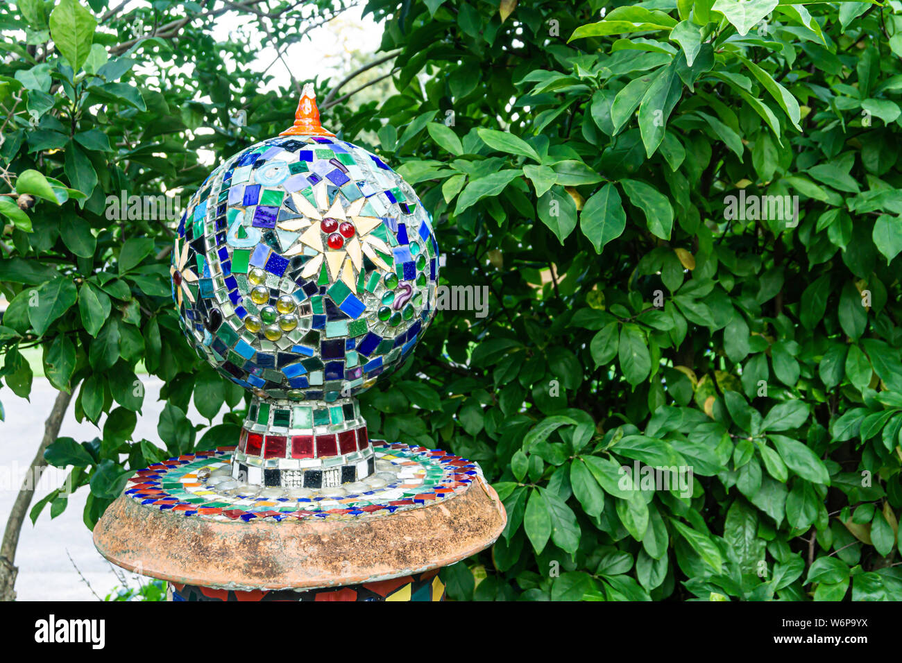 Mosaic globe on pedestal in suburban landscape with leaves in background, copy space, colorful patterns, glass tiles, objet d'art, outdoor art Stock Photo