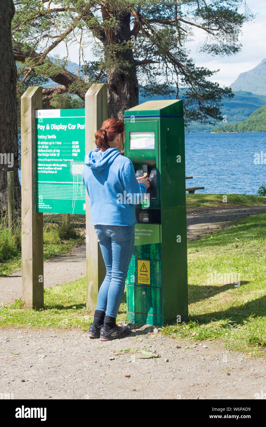 A woman buys a car park ticket from a ticket machine in the Lake District National Park. UK Stock Photo