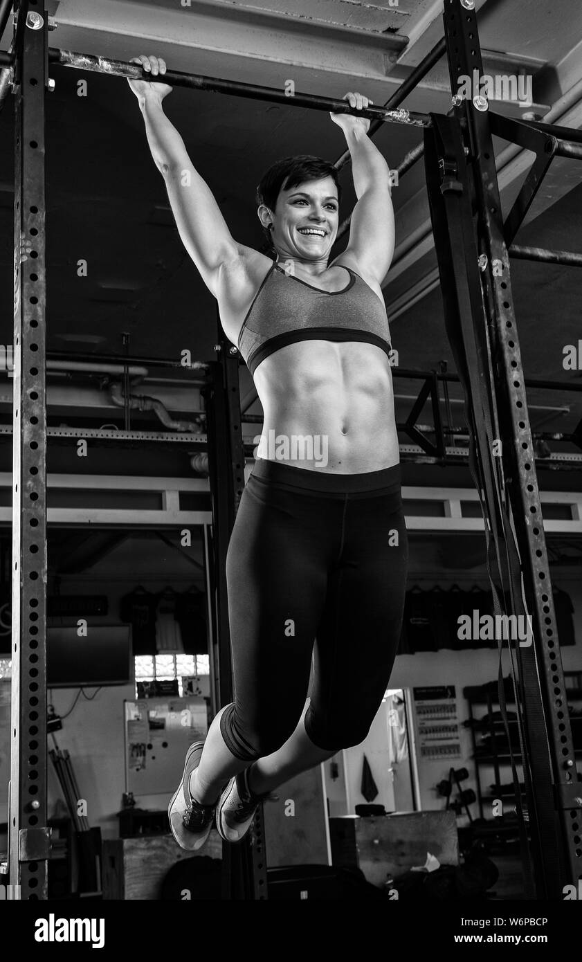 A young beautiful woman with abs is doing toes to bar at the horizontal bar. The short haired sporty athlete is doing a functional fitness workout. Stock Photo