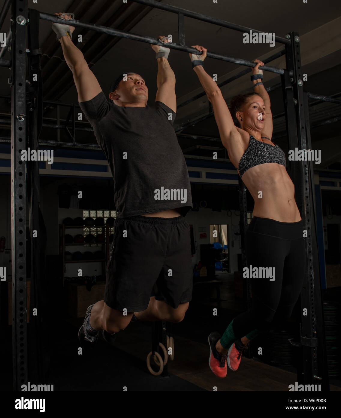 An athletic young couple is doing a fitness training together and having fun. Muscular man and woman are doing the exercise toes to bar. Stock Photo