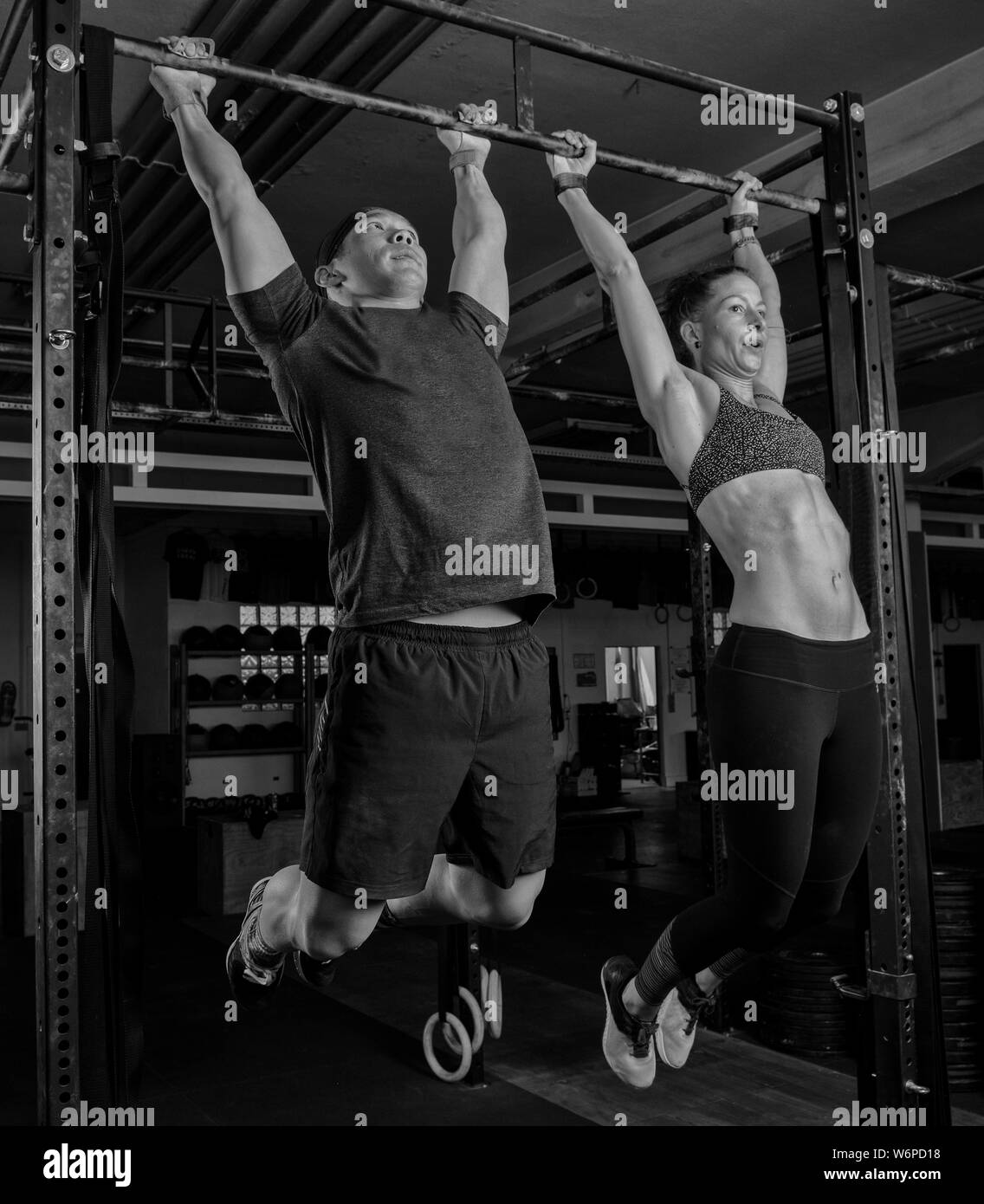 An athletic young couple is doing a fitness training together and having fun. Strong man and woman are doing the exercise toes to bar. Stock Photo