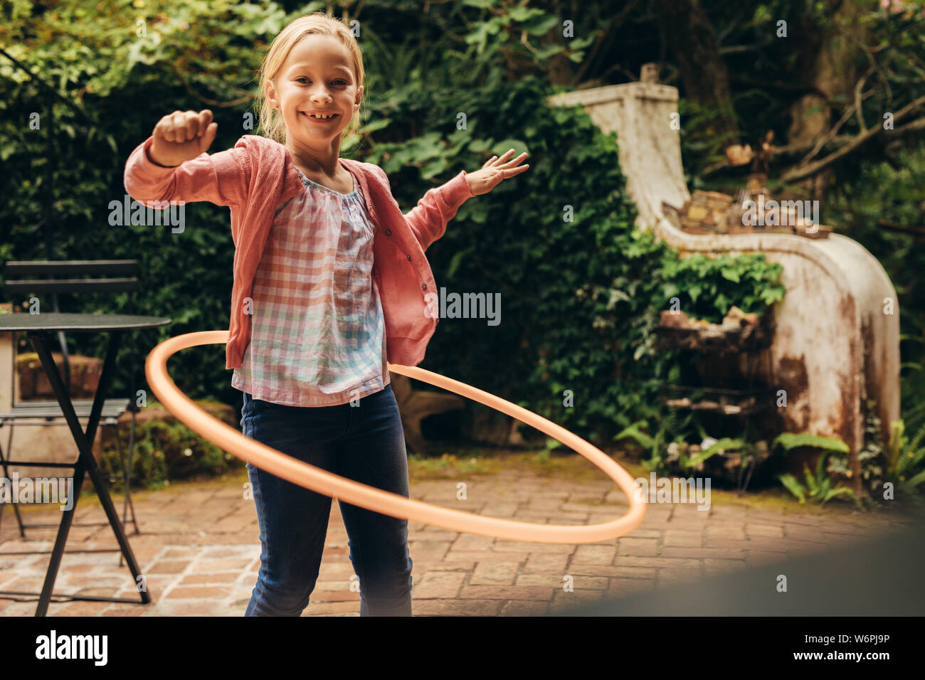 Smiling kid playing with a hula hoop in her backyard. Girl having fun  turning a hoopla ring around her waist Stock Photo - Alamy