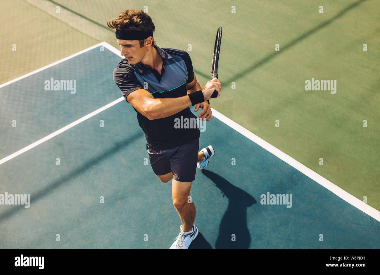 Focused young male tennis player hitting a forehand. Tennis player playing a match on hard court. Stock Photo