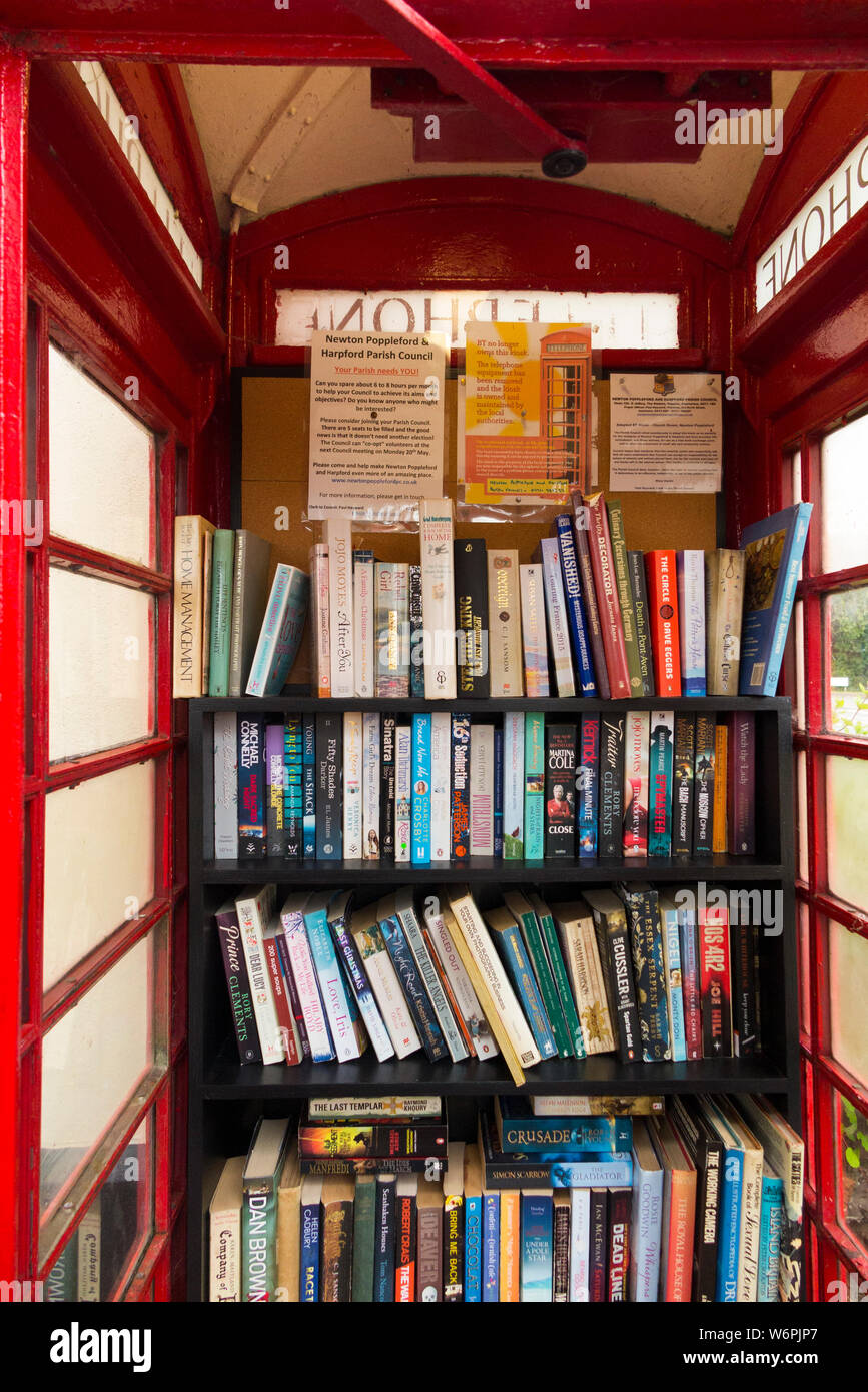Books on shelves forming a little local library in an old red phone box / kiosk / call box in Newton Poppleford, Devon. England UK  (110) Stock Photo