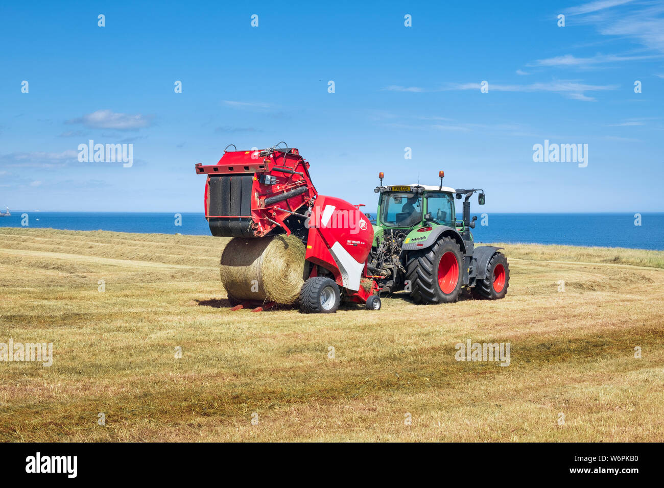 Modern farming machinery - a farmer in tractor making circular hay bales with a  Lely Welger RP 445  an advanced variable round baler. Stock Photo