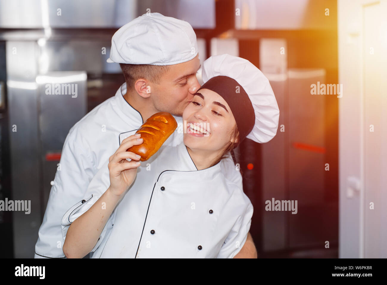 Boy baker kisses a girl on the cheek in a bakery against the background of the oven. Stock Photo