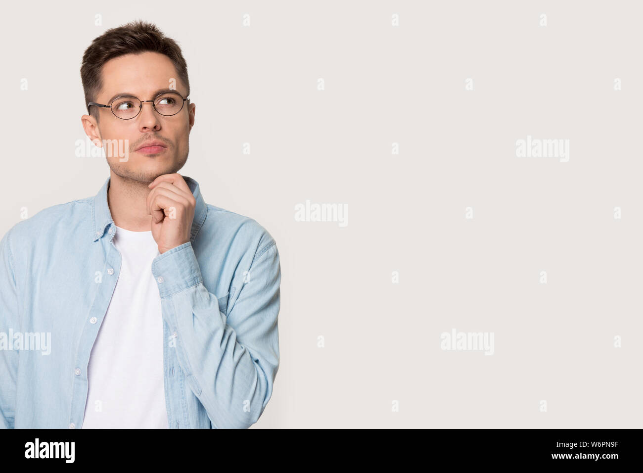 Pensive thoughtful young man pose on grey background looking aside Stock Photo